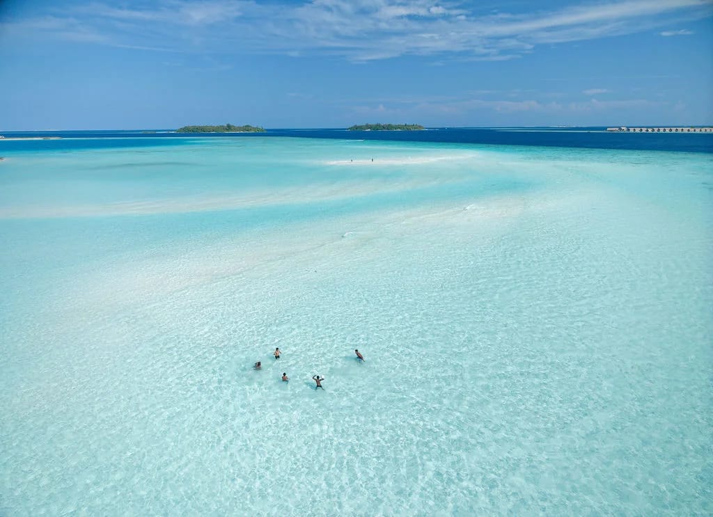 Swimmers in a clear turquoise lagoon beneath a wide blue sky
