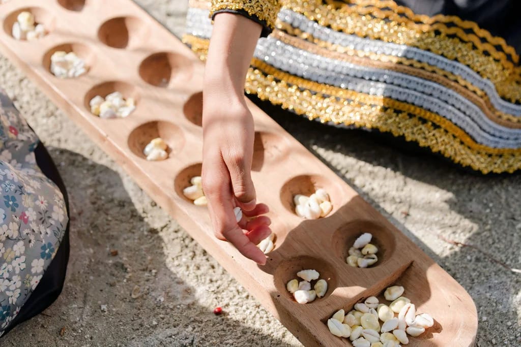 Hands moving shells around the hollows of a wooden game board