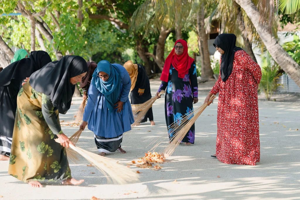 A closer view of residents gathering fallen leaves with traditional brooms