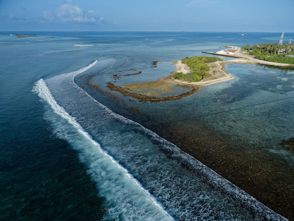Aerial view of white waves curling around a reef beside the island