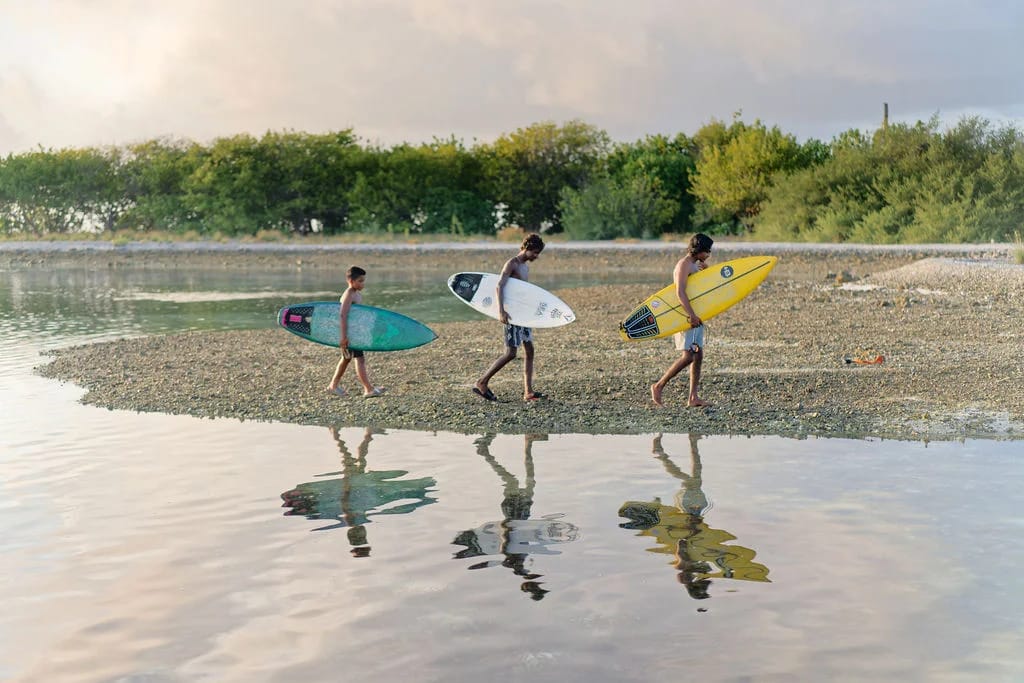Three surfers carrying colourful boards along the water's edge