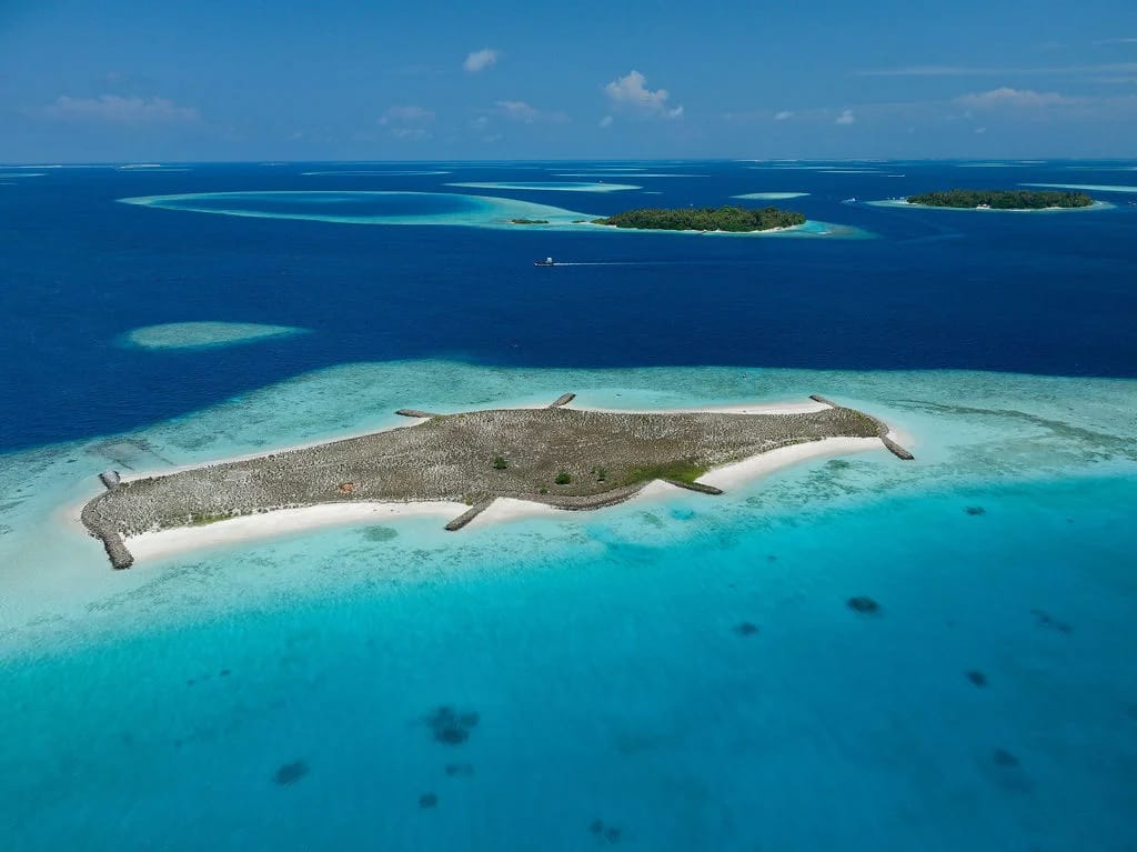 A sandy island surrounded by turquoise shallows and deep blue channels