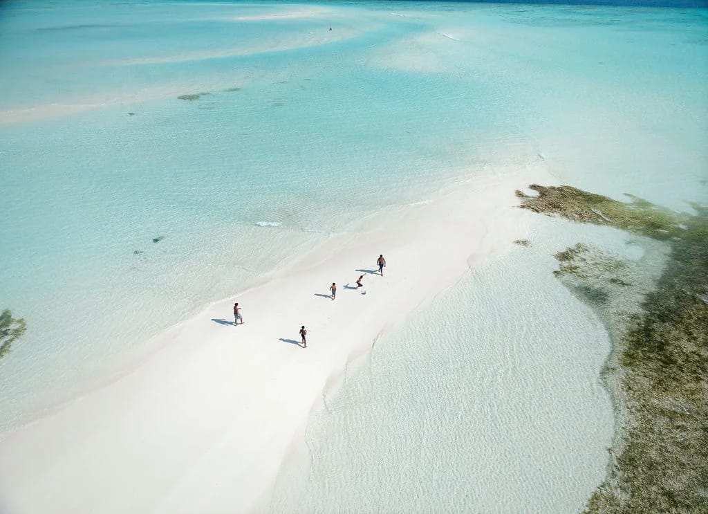 People walking along a white sandbar surrounded by shallow turquoise water