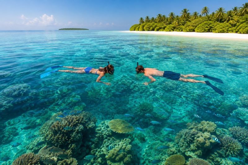 Two travellers snorkelling respectfully above a coral reef in a clear Maldivian lagoon