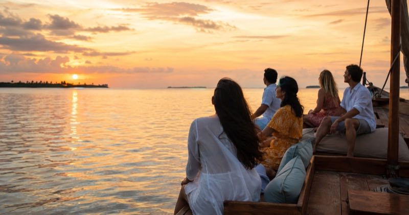 Travellers watching a Maldivian sunset from a traditional wooden dhoni